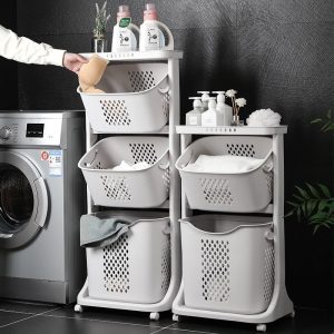 Giỏ đựng đồ giặt 2 tầng màu trắng, đặt cạnh máy giặt, chứa quần áo và đồ dùng phòng tắm.