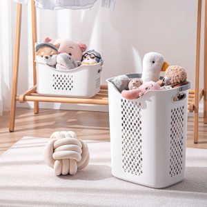 Giỏ đựng quần áo trắng, chứa đầy thú nhồi bông, đặt cạnh giá treo đồ.