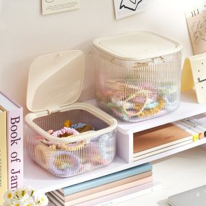 Hai hộp nhựa trong suốt đựng phụ kiện tóc đặt trên kệ sách.