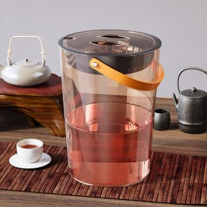Thùng đựng bã trà trong suốt có quai xách, đặt trên bàn trà.