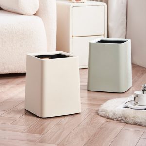 Thùng rác nhựa PP 2 lớp nắp lật chống rò rỉ cho gia đình 23L Hai thùng rác nhựa hình vuông và tròn đặt cạnh sofa, màu trắng kem và xanh nhạt.