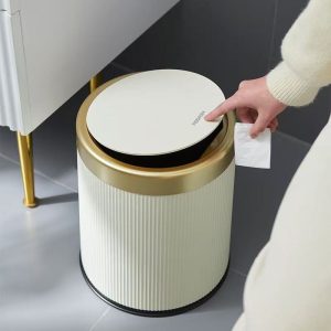 Người dùng nhấn nắp thùng rác màu trắng kem viền vàng trong phòng tắm hiện đại.