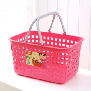Giỏ nhựa màu hồng lớn với hai tay cầm chắc chắn đặt trên bàn cạnh cửa sổ.