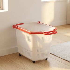 Giỏ nhựa trắng có bánh xe và tay cầm đỏ đặt sát tường.