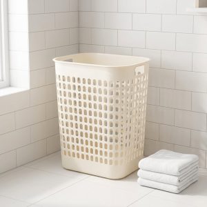 Giỏ đựng quần áo nhựa PP thoáng khí chống ẩm mốc đa năng Giỏ đựng quần áo màu kem đặt trong phòng tắm, bên cạnh là chồng khăn sạch.