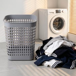 Giỏ nhựa xám đặt cạnh máy giặt, bên cạnh là quần áo bẩn.