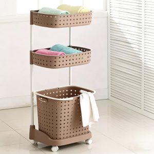 Giỏ đựng đồ giặt 3 tầng màu nâu có bánh xe đặt cạnh cửa sổ.