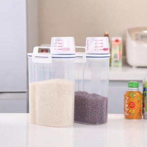 Hai hộp đựng thực phẩm đặt trên bàn bếp, chứa gạo và đậu đỏ, nắp có vạch chia tiện lợi.