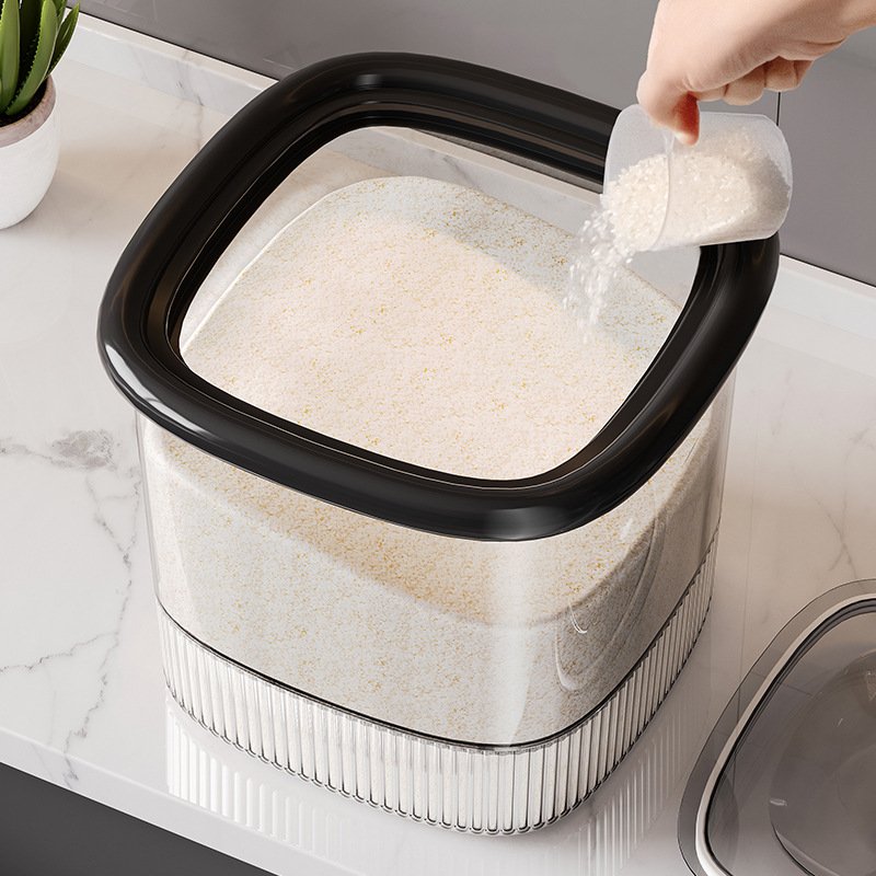 Thùng gạo thông minh nhựa PP dung tích lớn 25kg kín khí chống ẩm Người đang đổ gạo vào hộp nhựa trong suốt nắp đen, đặt trên mặt bàn.
