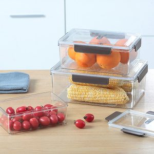 Ba hộp nhựa đựng cam, ngô, cà chua đặt trên bàn bếp.