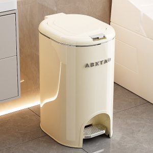 Thùng rác đạp chân màu kem đặt cạnh tủ trong phòng tắm, nắp đóng kín.