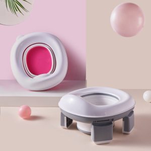 Bô vệ sinh di động gấp gọn nhựa ABS cho bé du lịch, dã ngoại, xe hơi Bô vệ sinh gấp gọn màu xám và hồng đặt cạnh tường.
