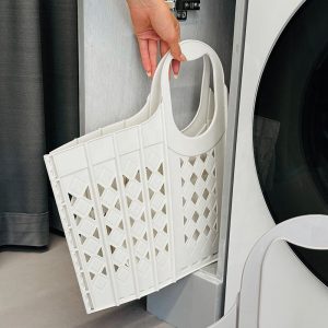Giỏ nhựa trắng được gấp gọn và cất vào khe nhỏ cạnh máy giặt.