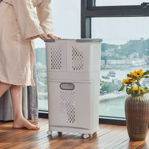 Giỏ đựng đồ giặt đặt cạnh cửa sổ, có bánh xe và hoa trang trí bên cạnh.