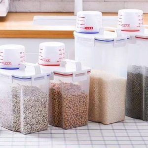 Các hộp đựng thực phẩm với nhiều kích cỡ, chứa các loại hạt và gạo, đặt trên bàn bếp.