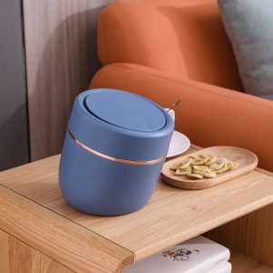 Thùng rác mini xanh dương đặt trên bàn cạnh ghế sofa.