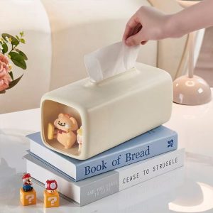 Hộp đựng khăn giấy màu kem đặt trên sách, bên trong là mô hình gấu và kem.