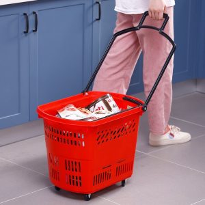 Người dùng kéo giỏ nhựa đỏ đầy thực phẩm bằng tay cầm kéo dài.