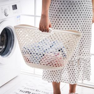 Người phụ nữ cầm giỏ đựng quần áo màu trắng, bên trong có quần áo.