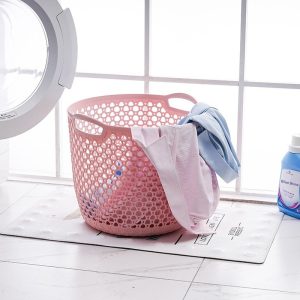 Giỏ đựng quần áo màu hồng đặt cạnh máy giặt, bên trong có quần áo.